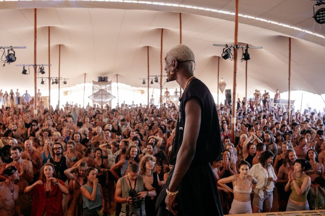 A packed tent seen from the back, the crowd facing the stage under warm lights