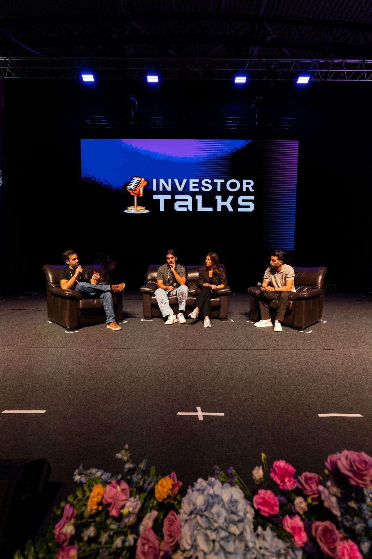 Four speakers in armchairs on stage under the Investor Talks screen